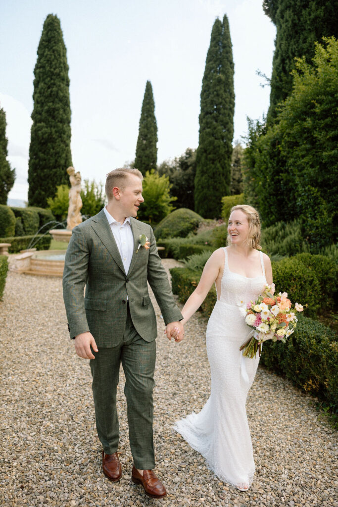 Bride and groom walking through garden paths of the historic villa after their elopement with stone architecture and olive trees.
