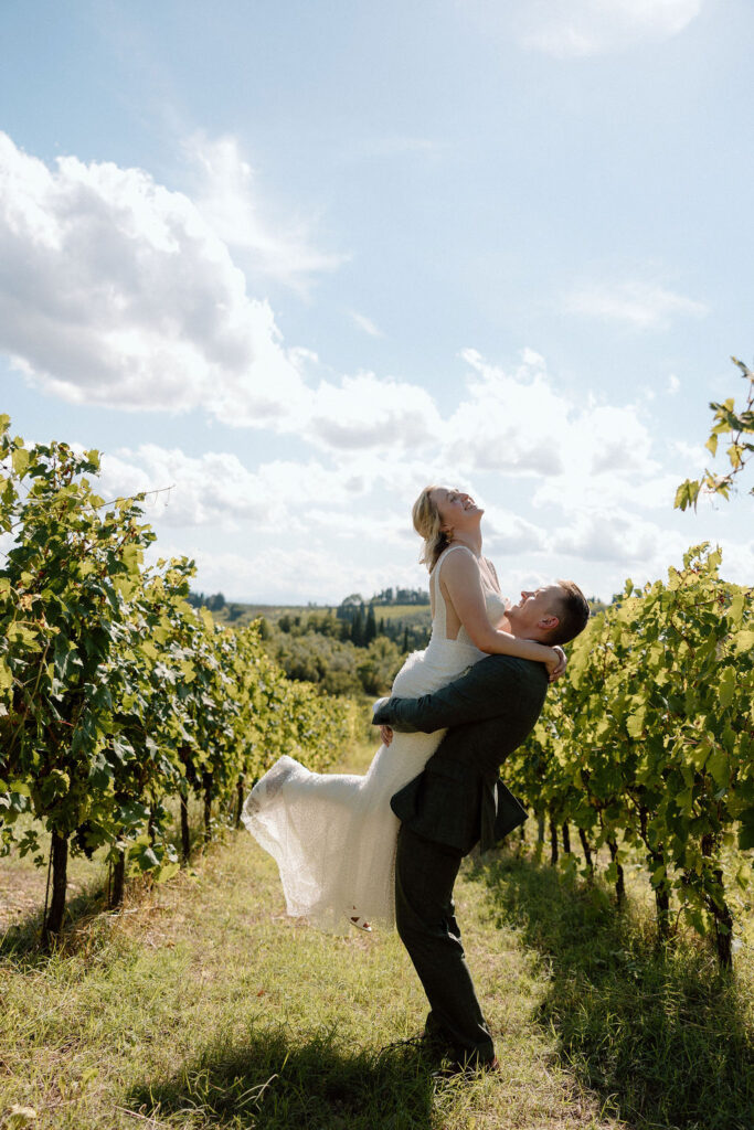 Bride and groom walking hand in hand through sunlit vineyards in Tuscany during an intimate Italian destination wedding.