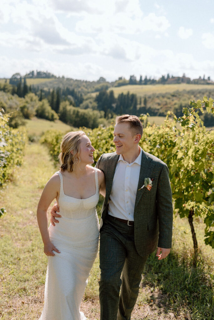 Bride and groom walking hand in hand through sunlit vineyards in Tuscany during an intimate Italian destination wedding.