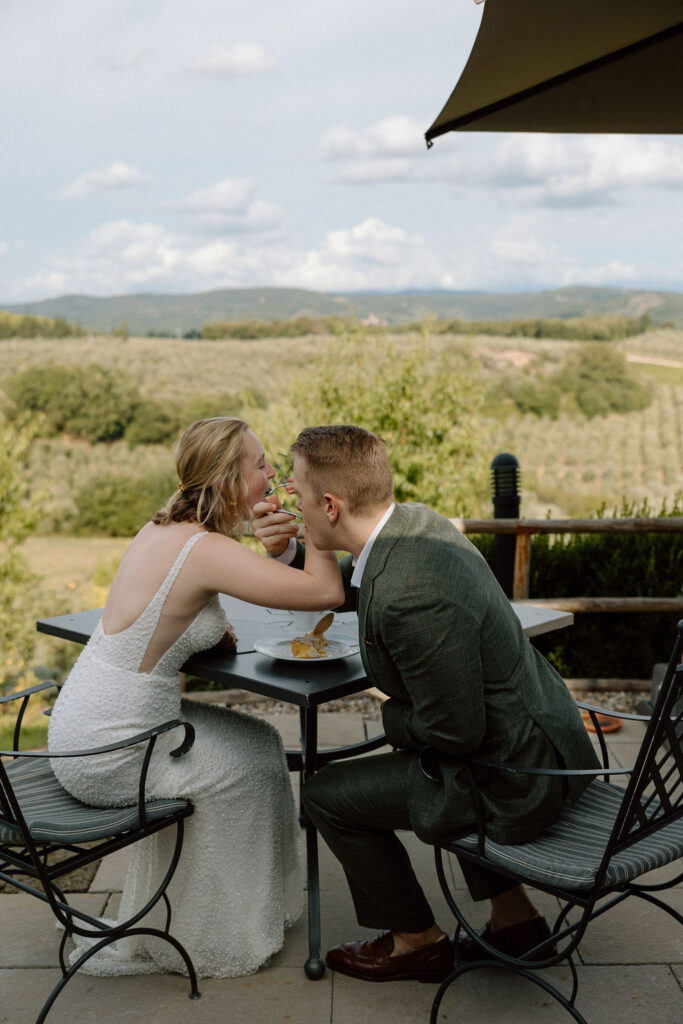 Couple cutting a small cake together in the Tuscan landscape after their elopement ceremony, captured in warm afternoon light.