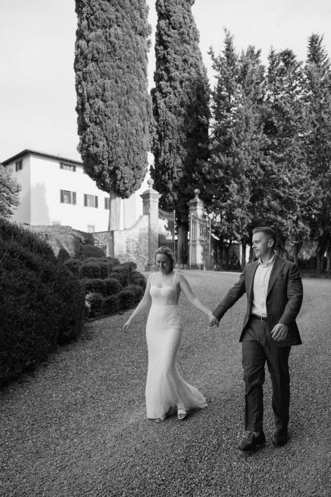 Bride and groom walking through garden paths of the historic villa after their elopement with stone architecture and olive trees.