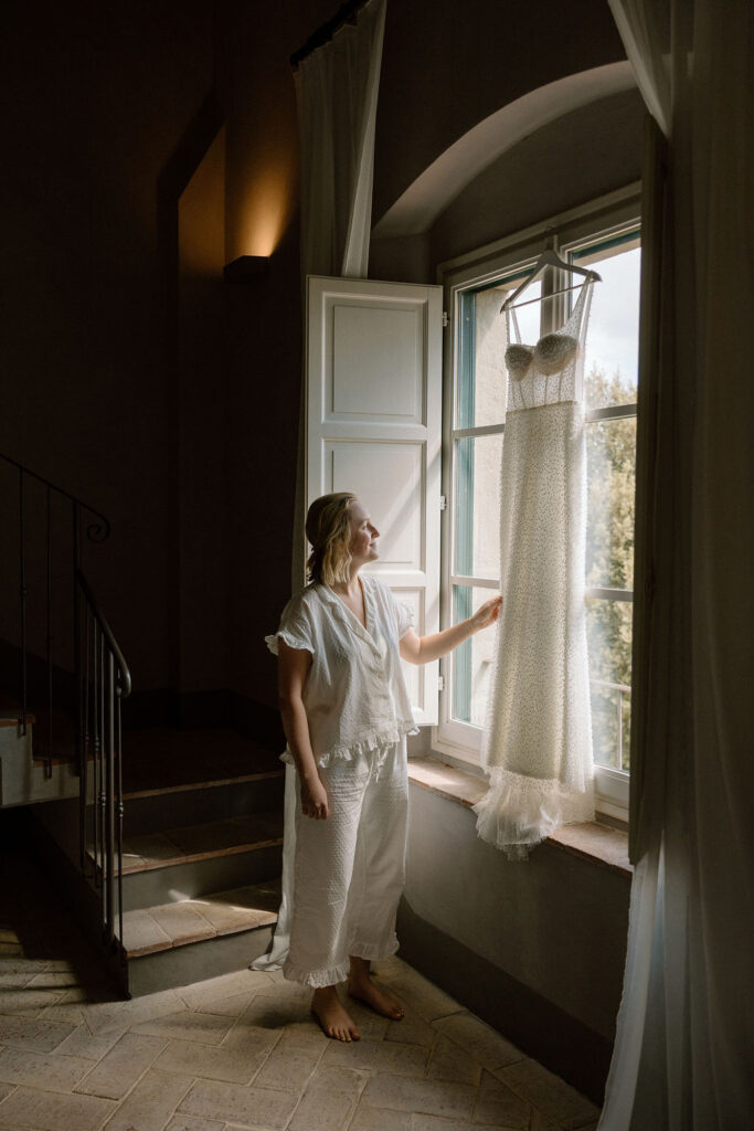 Bride adjusting her wedding dress while getting ready in a Tuscan villa before her private elopement ceremony.