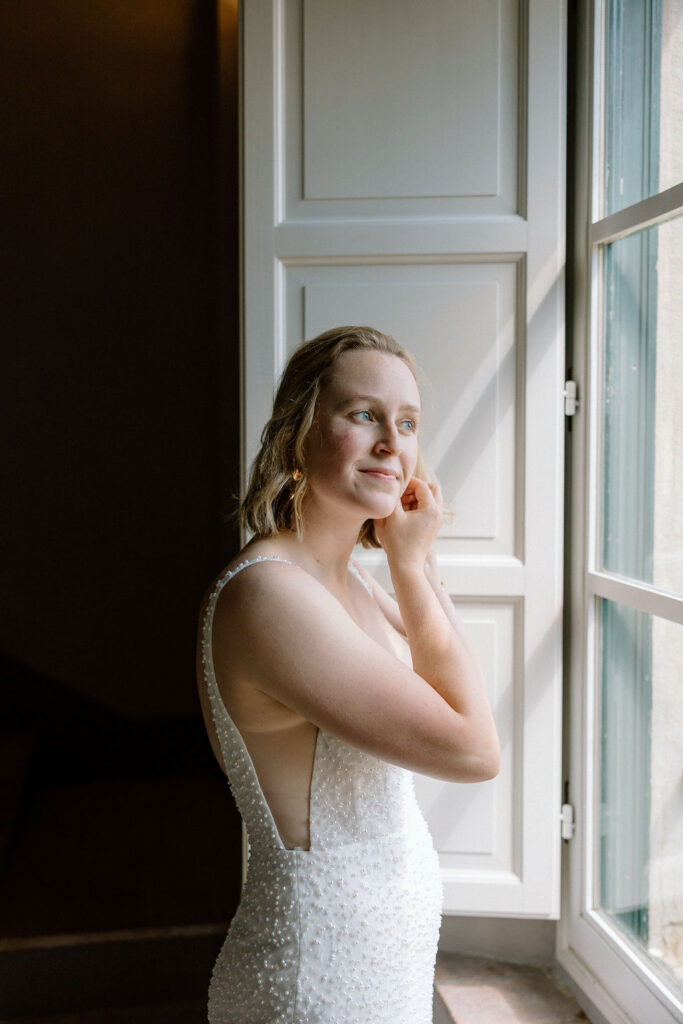 Bride getting ready for her Tuscan elopement, wearing a lace wedding gown in soft natural light inside a countryside villa.