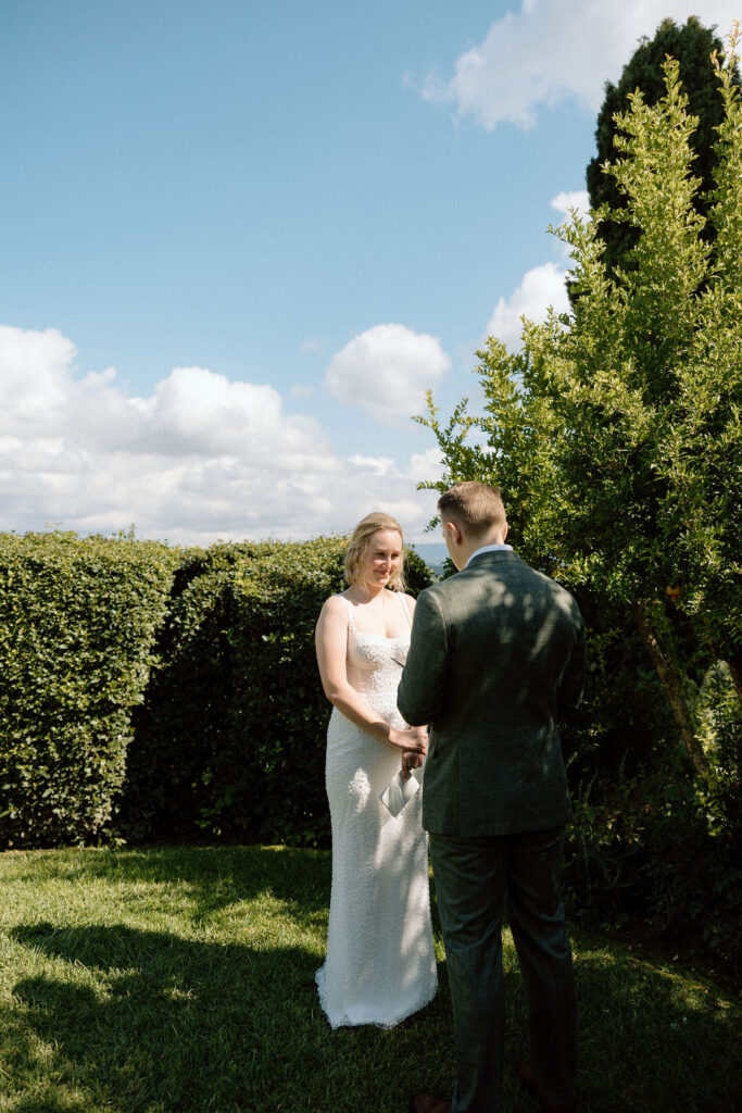 Intimate Tuscan elopement ceremony with the bride and groom exchanging vows surrounded by rolling hills and countryside views in Italy.